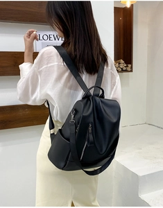 Side view of black PU leather backpack showing silver zippers and side pockets on model