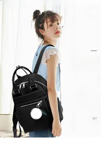Détail du sac à dos noir en nylon oxford avec fermetures argentées et pompon blanc