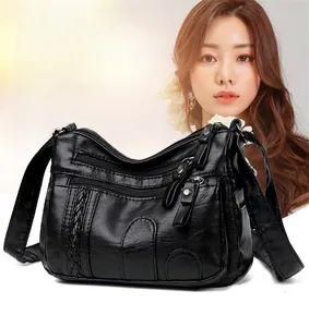 Detail of black pebbled faux leather crossbody bag featuring multi-zipper compartments