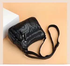 Detail view of black soft leather crossbody bag with multiple zippers and curved stitching