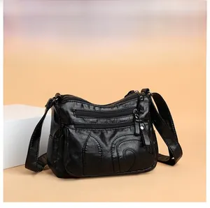 Close-up of soft black PU leather crossbody bag with multi-pocket zippers and texture