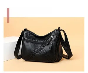 Detail of black pebbled PU leather crossbody bag with multiple zippers and V-shaped braids