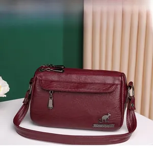 Detailed close-up of wine red soft leather crossbody bag with multiple zippers and texture