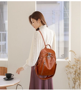 Detailed view of a brown leather backpack with multiple metal zippers and slim straps