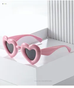 Detail of pink heart-shaped Y2K sunglasses on white geometric display blocks