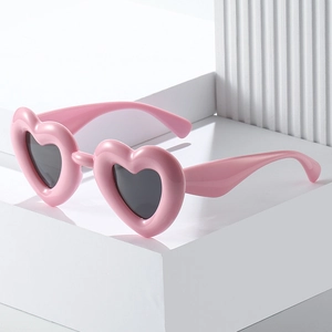 Pink heart-shaped Y2K sunglasses with dark lenses on minimalist decorative pedestal