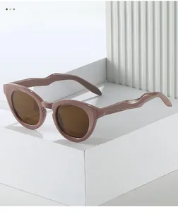 Detail of trendy oval sunglasses with pink wavy frames and dark brown lenses on white props