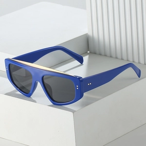 Oversized royal blue sunglasses with gold metal top bar and grey lenses on white blocks