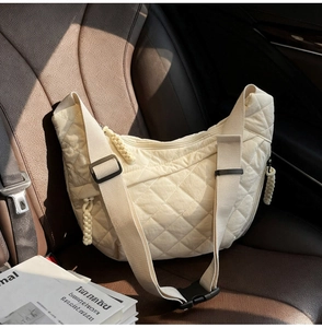 Dettaglio borsa a mezzaluna beige trapuntata con tracolla larga sul sedile dell'auto
