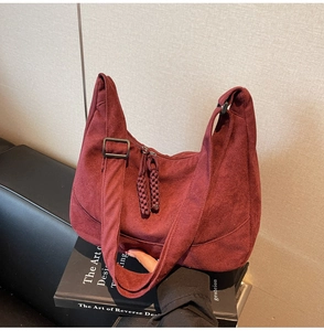 Dettaglio della borsa a spalla in camoscio bordeaux con tracolla larga e nappe lunghe