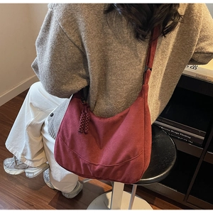 Borsa hobo in tela bordeaux indossata a spalla in una biblioteca vintage