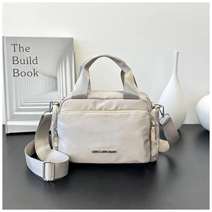 Close-up of beige nylon tote bag with multiple zipper pockets and metal brand logo