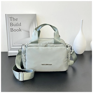 Detailed view of light green nylon tote bag featuring metal logo and adjustable strap