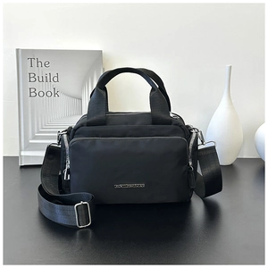 Detail of black nylon tote bag with front zipper pocket and silver metal logo hardware