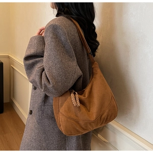 Dettaglio borsa hobo in camoscio marrone con pendenti intrecciati su cappotto grigio
