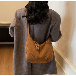 Dettaglio borsa a mezzaluna in camoscio marrone con zip intrecciata su cappotto