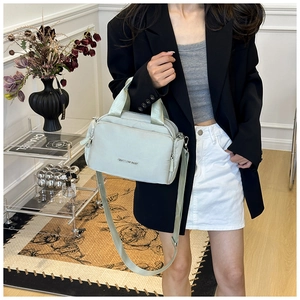 Detail of mint green multi-pocket tote bag featuring adjustable strap and silver logo plate