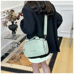 Detail of light green nylon tote bag featuring wide shoulder strap and metal logo plaque