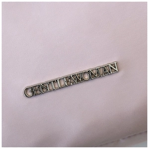 Detail shot of the silver metal Gentlewoman logo on high-quality light purple twill fabric