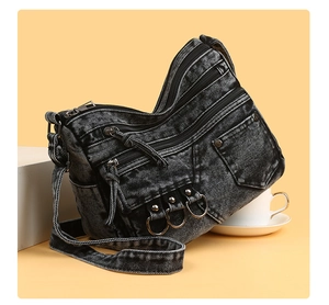 Close-up of washed denim crossbody bag featuring multiple zipper pockets and metal ring details