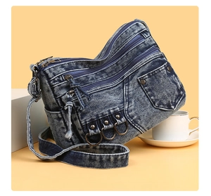 Detail of washed denim crossbody bag featuring multiple zipper pockets and metal rivets
