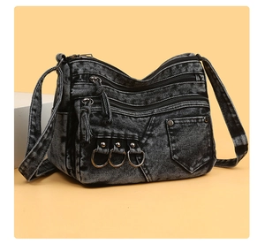 Macro detail of washed denim crossbody bag featuring utility zippers and metal rings