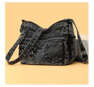 Detail of washed denim crossbody bag featuring multiple functional zippers and metal rivets