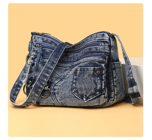 Close-up of vintage washed denim crossbody bag with multiple zippers and silver hardware