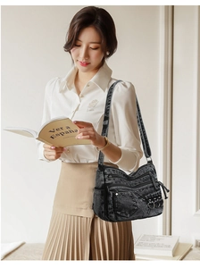 Detail of washed black denim crossbody bag with multiple zippers and metal ring accents