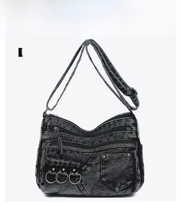 Detailed front view of washed denim crossbody bag with multiple zippers and metal rings