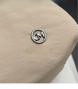 Macro shot of silver CM metal logo on beige high-density fabric tote bag