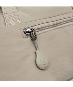 Detail of light beige crossbody bag showing CHUANGMI branded zipper pull and fabric texture