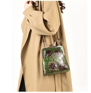 Detalle de bolso verde con cierre de boquilla, diseño floral y correa de cadena en modelo
