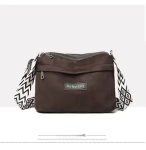 Detail of dark brown suede crossbody bag featuring multi-zipper layers and geometric strap