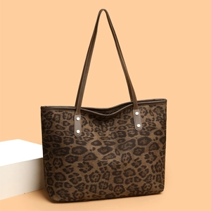 Large leopard print tote bag with brown leather handles on a warm orange background