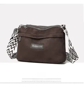 Detail of dark brown suede crossbody bag with geometric woven strap and zipper