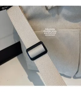 Detail of adjustable off-white woven strap and black buckle on beige corduroy bag