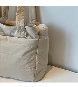 Detail view of the nylon tote bag side pocket with a beige thermos for capacity display