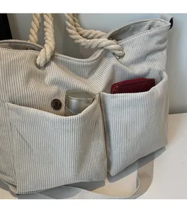 Detail of off-white corduroy tote bag showing front pockets and woven rope handles