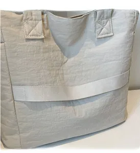 Detail view of the quilted tote bag showing a functional trolley sleeve for luggage attachment