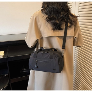 Detail of black nylon crossbody tote bag showing front zip pocket and shoulder strap on model