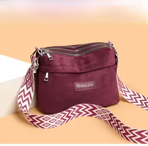 Detail of burgundy crossbody bag with multiple zippers and geometric patterned strap