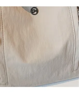 Detailed macro shot of light beige nylon fabric with a black CM metal logo and fine stitching