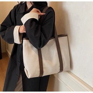 Side view of large canvas tote bag with brown leather trim shown on model shoulder