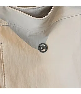 Detail of a beige nylon bag featuring a round black metal CM logo and fine fabric texture
