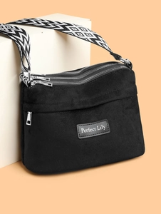 Detail of black nylon crossbody bag with three silver zippers and geometric patterned strap
