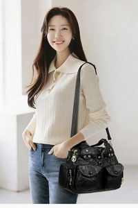 Detail of a black multi-pocket shoulder bag with gold rivets and adjustable strap