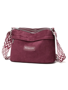 Detail of burgundy suede shoulder bag showing multi-zipper layers and woven geometric strap