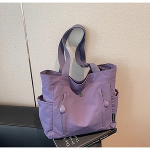 Detailed view of a purple nylon tote bag featuring front zippers and a side brand label
