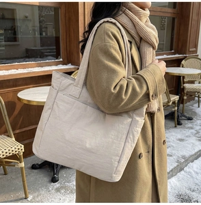 Detail of a beige nylon tote bag with wide straps shown in a winter outdoor setting